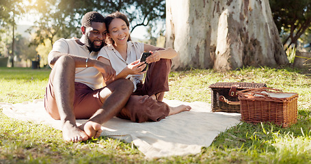 Image showing Happy, social media and an interracial couple on a picnic with a phone for communication, tech or an app. Talking, summer and a black man and woman with a mobile for a chat on a date in a park