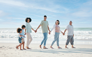 Image showing Summer, beach and a family holding hands while walking on the sand by the ocean or sea together. Grandparents, parents and children outdoor in nature for travel, vacation or holiday on the coast