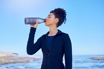 Image showing Fitness, woman and drinking water at beach for running, health or morning cardio on blue sky by an ocean. Exercise, hydration and thirsty lady runner with sports liquid after training or sea workout