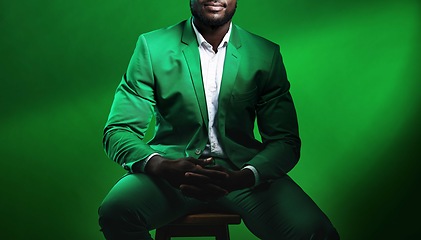 Image showing Fashion, suit and black man model with a formal outfit sitting on a chair while posing in a studio. Elegant, trendy and African male in luxury, stylish and fancy clothes isolated by green background.