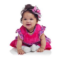 Image showing Innocent, cute and happy baby girl in a studio with a floral, beautiful and flower outfit and headband. Happiness, smile and infant child sitting and playing while isolated by a white background.