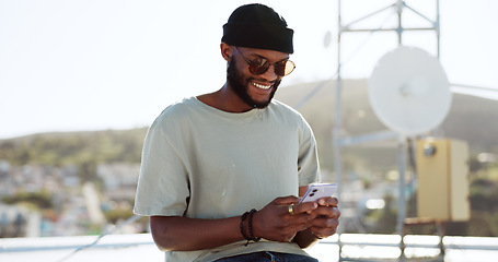 Image showing Phone, texting and happy black man on rooftop of city building using smartphone for social media, chatting and communication. Fashion, meme and young trendy guy typing message, text or post in town