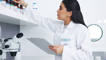 Image showing Medical researcher checking bottles with chemicals inside a modern science lab. Young focused scientist or pharmacist looking at hazardous and dangerous inventory while writing notes in a pharmacy