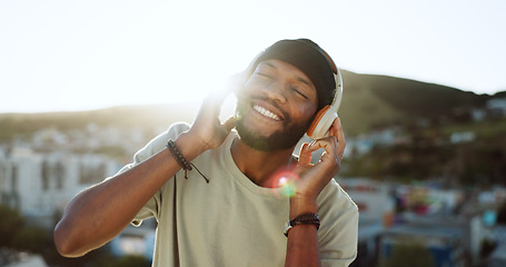 Image showing Man, music and dancing on rooftop with headphones in sunshine, city and summer with smile. Happy, black man and streaming to listen on internet, web or app to relax, dance and radio in Cape Town