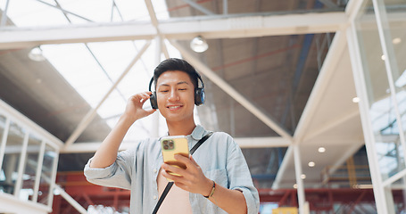 Image showing Phone, music headphones and Asian man walking in mall streaming podcast or radio. Technology, travel and happy male listening to song, audio sound or playlist on mobile smartphone in urban building.