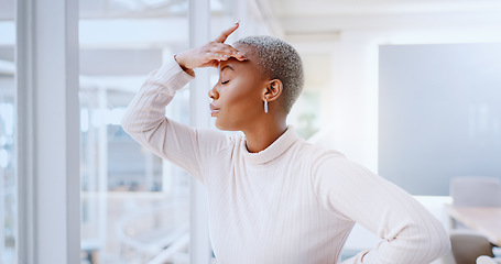 Image showing Young african american business woman suffering from a headache while standing in her office alone at work. Stressed black female business person looking tired while putting in overtime late at night