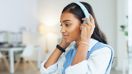 Image showing Young Indian creative with headphones sitting alone in an office and smiling. Copywriter looking pleased with her works as she types. Graphic designer uses music for motivation focusing on her task