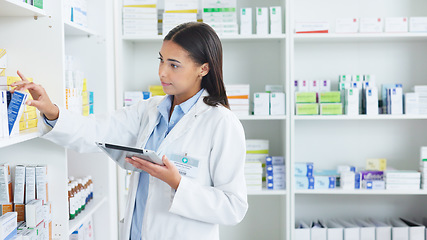 Image showing A young female pharmacist stocktaking in a dispensary using a tablet. Doctor preparing prescriptions and medication at clinic or pharmacy. Healthcare professional sorting medicine with digital device