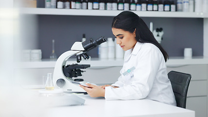 Image showing Young scientist using a digital tablet and microscope in a lab. Female pathologist analyzing medical samples while doing experiments to develop a cure. Microbiologist conducting forensic research