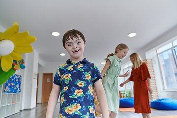 Image showing Small nursery school children with female teacher on floor indoors in classroom, doing exercise. Jumping over hula hoop circles track on the floor.