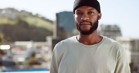 Image showing Black man, serious and portrait on rooftop in city, wind or confident in summer on holiday. Young, man and buildings in urban, metro or town with proud, sunshine and beard with focus, vision or dream