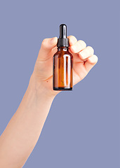 Image showing Hands, skincare and serum bottle in studio isolated on a purple background. Product, dermatology and woman or female model with hyaluronic acid, essential oil or cosmetics for aesthetics and beauty.