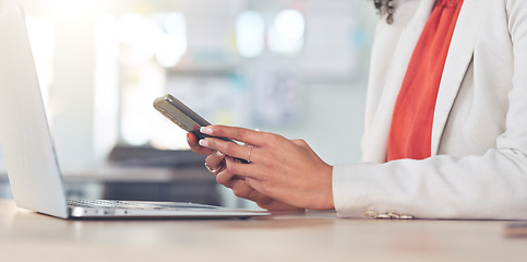 Image showing Closeup of fashionable business woman checking emails or fingers scrolling on app while working on a laptop in a modern office. Hands browsing online holding a phone and sitting at a desk inside.