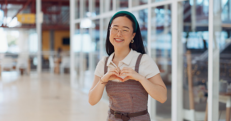 Image showing Face, heart and business woman with hand sign in office building, smile and happy for startup success. Asian girl, hand and emoji icon by excited business owner smiling for company vision in Japan