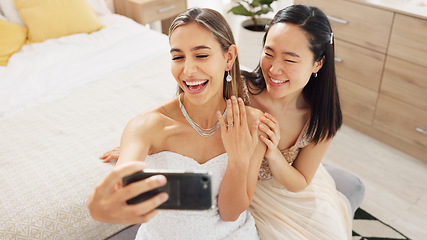 Image showing Bride, bridesmaid and selfie with phone, wedding and ring with a smile to post on social media. Happy woman and asian friend excited for marriage celebration with fashion white dress in a bedroom