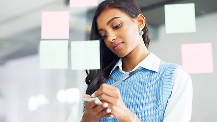 Image showing Young business woman brainstorming and planning a mind map while writing ideas on sticky notes on a glass wall in an office. Focused designer analyzing a marketing strategy and solutions for projects