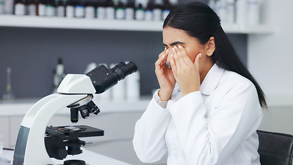 Image showing Female scientist looking through microscope and rubbing her eyes while suffering from eye strain or discomfort. Stressed biotechnology specialist does analysis of test sample in medical lab