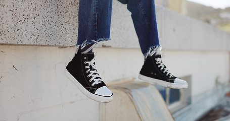 Image showing Rooftop, shoes and man in an urban city sitting on the top of a building for a view of the cityscape. Hipster, freedom and closeup of male feet with sneakers hanging from an outdoor roof in town.