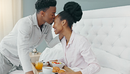 Image showing Breakfast in bed, love and black couple being romantic on their honeymoon, birthday or anniversary in a hotel room. Happy man kissing woman on head to express love and care while bonding in bedroom