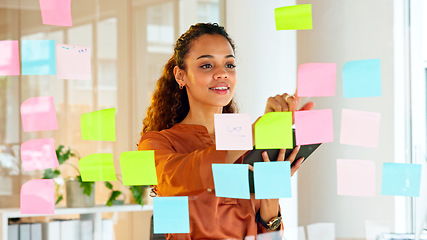 Image showing Happy female designer planning ideas on a glass wall with colorful sticky notes inside a creative and modern office. Busy woman enjoying her job while brainstorming projects and managing projects