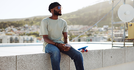 Image showing Black man, relax and rest on wall with skateboard on building rooftop in city. calm, serene and young happy trendy skater guy with phone chill freedom adventure outdoors in bokeh town background