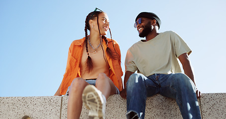 Image showing Couple, city and relax with a black man and woman sitting on a wall outdoor against a clear blue sky together. Street style, travel and love with a happy male and female bonding outside during summer