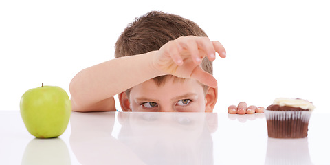 Image showing Cupcake, apple and child with food choice between unhealthy junk food and healthy nutrition product. Table, studio and kid boy decision between fruit and chocolate candy isolated on white background