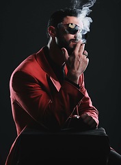 Image showing Fashion, smoking and red with a man model in studio on a dark background wearing a suit for style. Smoke, mafia and edgy with a handsome young male posing on black space holding a cigarette