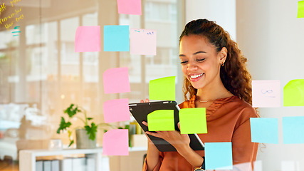 Image showing Focused female designer planning ideas on a glass wall with colorful sticky notes inside a modern and creative office. Busy woman enjoying her job while brainstorming projects and managing projects
