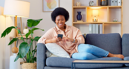 Image showing Laughing woman listening to music and sending a message with funny memes on her phone and drinking coffee while on the sofa. Happy black female browsing social media and surfing the internet online