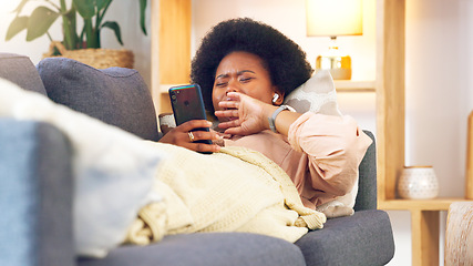 Image showing Bored and tired woman lying on a couch typing on her phone at home. A young African female relaxing and yawing on a sofa in her house on a boring weekend. A sleepy lady scrolling social media