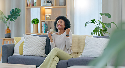 Image showing African woman celebrating a new job while sitting at home on a couch. A young females loan is approved via an email on her phone. A happy and excited lady cheering for a promotion on a sofa