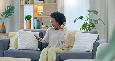 Image showing African woman celebrating a new job while sitting at home on a couch. A young females loan is approved via an email on her phone. A happy and excited lady cheering for a promotion on a sofa