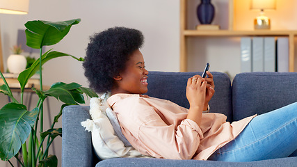 Image showing A laughing young woman texting on a phone at home. Cheerful female chatting to her friends on social media, browsing online and watching funny internet memes while relaxing on a sofa