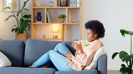 Image showing Relaxed Black woman listening to a podcast while drinking coffee and sitting on a couch at home. Happy African American woman streaming online content, enjoying an audiobook while laughing