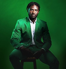 Image showing Fashion, formal and portrait of a black man in a suit sitting on a chair in studio with a luxury outfit. Elegant, stylish and African male model with fashionable clothes isolated by green background.