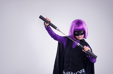 Image showing Little girl, halloween and superhero dress up with nunchucks for fighting against a grey studio background. Portrait of isolated girl playing super hero with martial art karate weapon and purple hair