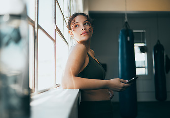 Image showing Thinking, phone and fitness with a sports woman by a window, standing in the gym during an exercise workout. Health, idea and a female athlete using social media or an app to track her training