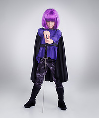 Image showing Little girl, superhero and halloween dress up posing with sword against a grey studio background. Portrait of girl child playing super hero with purple hair, costume or cosplay of a warrior vigilante