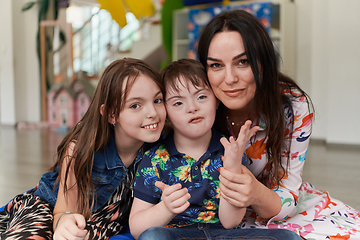 Image showing A girl and a woman hug a child with down syndrome in a modern preschool institution