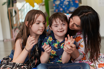 Image showing A girl and a woman hug a child with down syndrome in a modern preschool institution