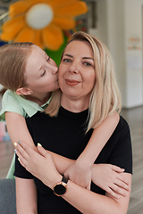 Image showing A cute little girl kisses and hugs her mother in preschool