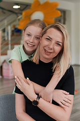 Image showing A cute little girl kisses and hugs her mother in preschool