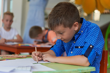 Image showing A boy at a preschool institution sits and draws in a notebook with a smile on his face