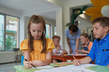 Image showing Creative kids during an art class in a daycare center or elementary school classroom drawing with female teacher.