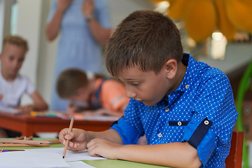 Image showing A boy at a preschool institution sits and draws in a notebook with a smile on his face