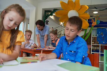 Image showing Creative kids during an art class in a daycare center or elementary school classroom drawing with female teacher.