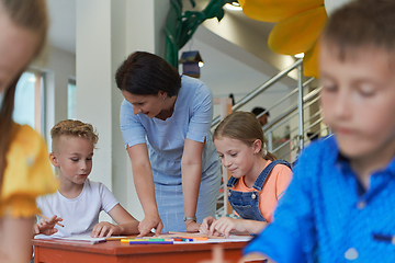 Image showing Creative kids during an art class in a daycare center or elementary school classroom drawing with female teacher.