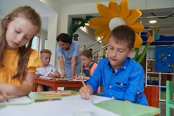 Image showing Creative kids during an art class in a daycare center or elementary school classroom drawing with female teacher.