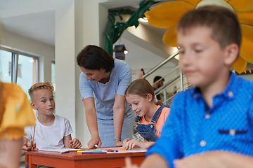 Image showing Creative kids during an art class in a daycare center or elementary school classroom drawing with female teacher.